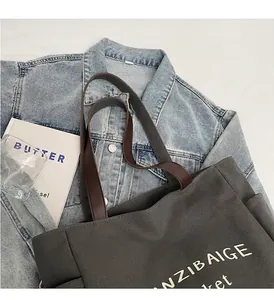 Detail van bruine lederen handvatten op een donkergrijze canvas tote bag met witte print