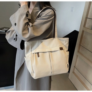 Detail of beige canvas tote bag showing side pocket and brown leather shoulder strap