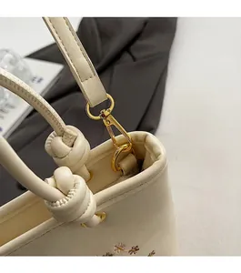 Détail des ferrures dorées et broderies florales sur le sac à main de couleur crème
