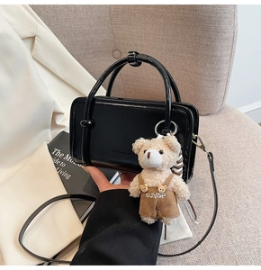 Detail of glossy black crossbody bag featuring a cute teddy bear charm on a soft sofa