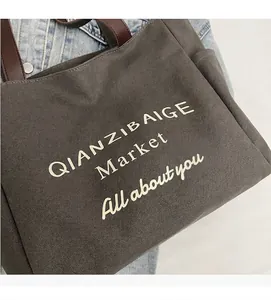 Detailopname van de grijze canvas draagtas met bruine leren hengsels en tekst