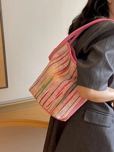 Pink tote bag with colorful vertical stripes and leather handles worn by a model