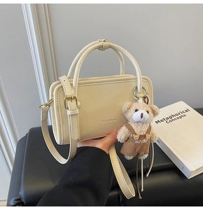 Detail of beige leather crossbody bag featuring a plush bear charm and metal logo