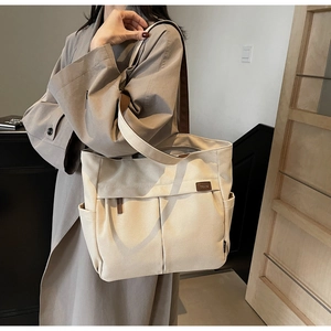 Detail of canvas tote bag with side pockets, brown straps, and leather brand logo