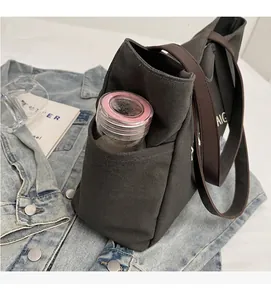 Detailopname van het zijvak van een grijze canvas tas met een roze glazen waterfles