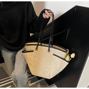 Detail of woven straw tote bag with black trim and side pockets holding decorative tulips