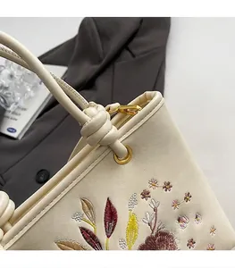 Détails de broderie florale et poignée nouée sur un sac seau élégant blanc cassé