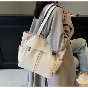 Detail of beige canvas tote bag showing front pleated pockets and leather brand patch