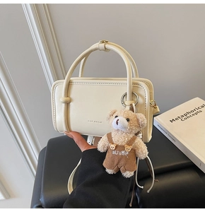 Detail of cream white rectangular handbag featuring embossed letters and a plush bear charm
