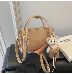 Detail of beige square handbag with smooth faux leather, gold hardware and plush bear charm