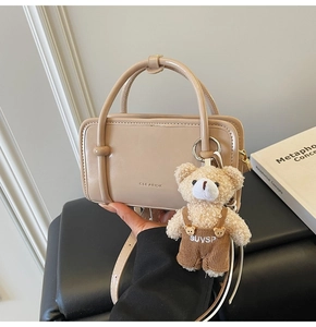 Detail of beige square handbag with dual handles and cute plush teddy bear charm