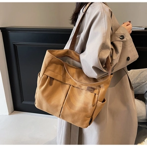 Detailed side view of large canvas tote bag with brown leather handles and side pockets