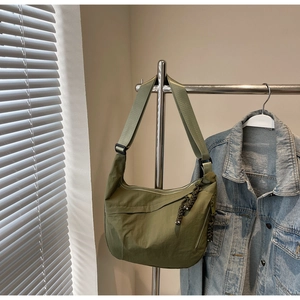 Detail of army green nylon crescent crossbody bag with woven knot charm on a metal stand
