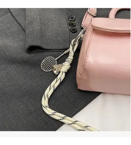 Pink leather handbag detail featuring a metal badminton racket pendant and woven cord