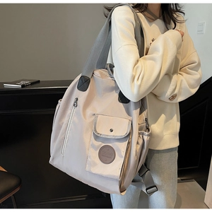 Detail of beige nylon travel backpack showing front buckle pocket and side storage compartment