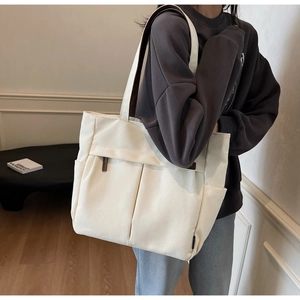 Detail shot of off-white canvas tote bag featuring large front pockets and brown leather accents
