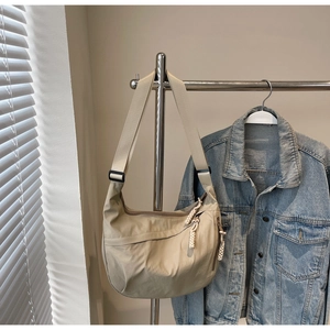 Detail view of beige nylon crescent bag with adjustable wide strap and woven zipper puller