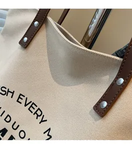 Detail of canvas tote bag showing brown leather handles and sturdy metal rivet stitching