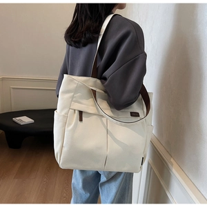 Detail shot of a large canvas tote bag with brown straps and side pockets on a model