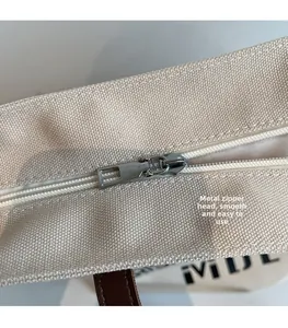 Detail of the smooth hardware zipper head and iViDE logo on the beige canvas tote bag