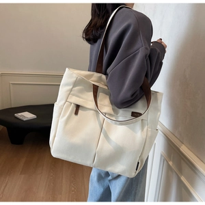 Detail of off-white canvas tote bag featuring reinforced brown straps and front pocket