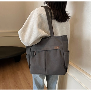 Close-up of dark grey canvas tote bag featuring double front pockets and brown leather label
