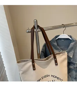 Detail of canvas tote bag with brown leather straps, metal rivets and slogan print