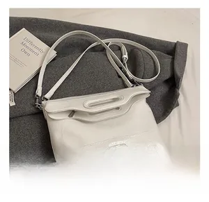 Detail view of white textured leather bucket bag with silver metal plate on grey fabric