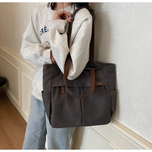 Detail of dark brown canvas tote bag with side pocket and side logo on model
