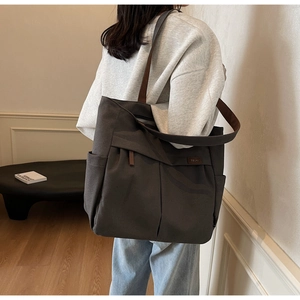 Close-up of charcoal canvas tote bag with brown leather straps and brand label detail