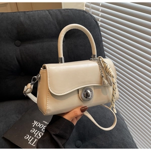 Detail of cream white small square bag featuring metal twist lock and woven tassel charm