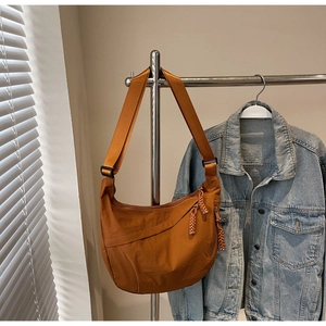 Detail of caramel nylon crescent bag featuring a woven rope zipper and wide strap