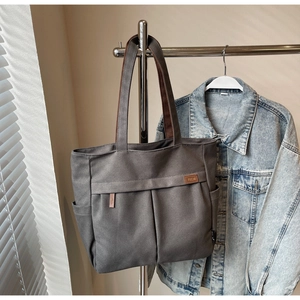 Detail of grey canvas tote bag featuring reinforced brown handles and functional side pockets