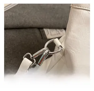 Detail of silver metal hook and textured white leather shoulder strap connection