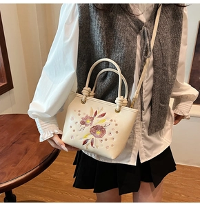 Détail de broderie florale sur sac à main crème porté par un mannequin en tenue décontractée
