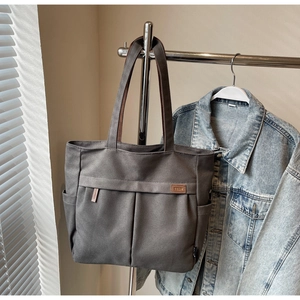 Detail of grey canvas tote bag featuring front pleated pockets and brown leather brand tag