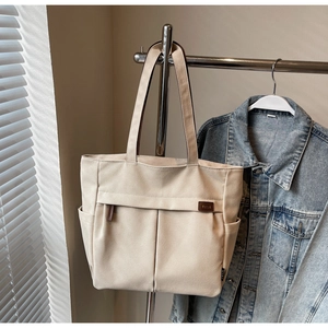 Detail of beige canvas tote bag showing outer pocket, side compartment and leather brand tag