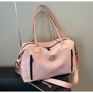 Detail of light pink travel bag showing matte texture, logo badge and black zippers