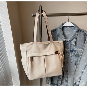 Detail of beige canvas tote bag with brown leather handles and dual front pockets