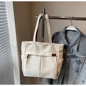 Detail of canvas tote bag showing front pockets and brown TELII leather brand patch