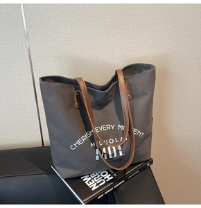 Detail of dark grey canvas tote bag with brown leather handles and printed white text
