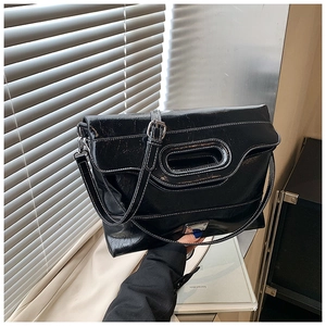 Detail of black glossy bucket bag with white contrast stitching and oval cutout handle