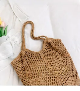 Close-up of brown woven tote bag with fringe details on a white fabric background