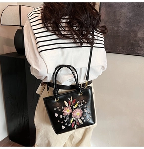 Détail de broderie florale sur un sac fourre-tout noir en cuir avec bandoulière