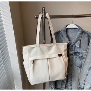 Detail of a large beige canvas tote bag with brown straps and zipper pockets shown in sunlight