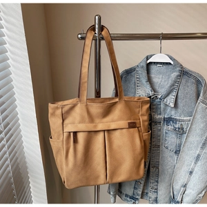 Detail of khaki canvas tote bag with front pockets and leather label on hanger