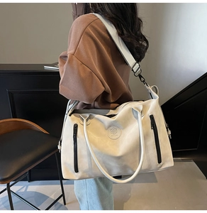 Close-up of beige travel tote with embossed logo and adjustable wide shoulder strap