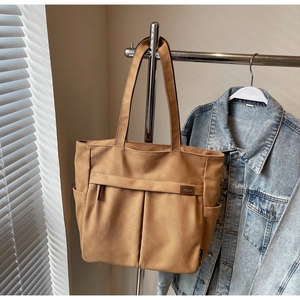 Detail view of khaki canvas tote bag featuring front zipper pockets and durable handles