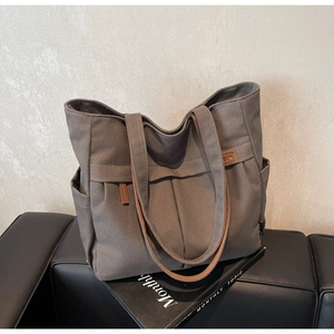 Detail of grey canvas tote bag featuring a leather logo patch and pleated design