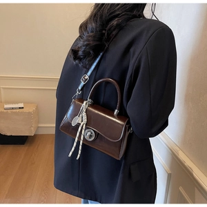 Detail of a dark brown vintage leather crossbody bag with a silver clasp and chic tassel